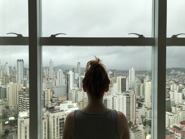 Žena stojí pred veľkým oknom a pozerá sa na mesto 